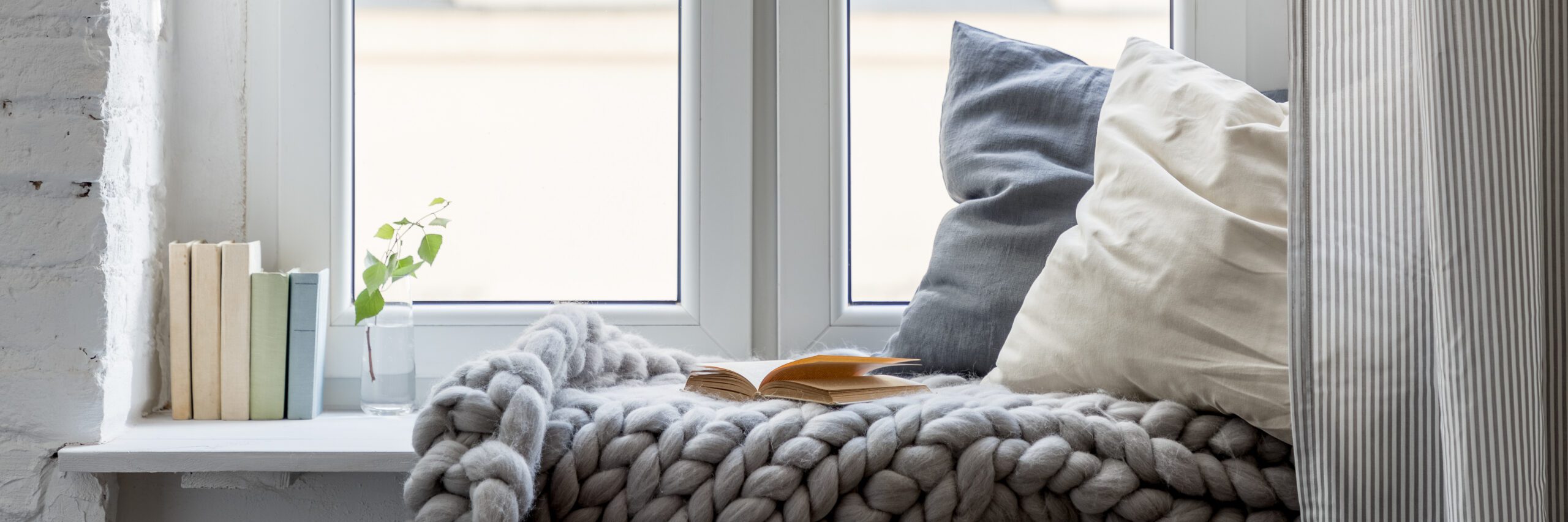 Hygge: Relaxation area with books, pillows and cozy blanket on a wooden windowsill, panorama