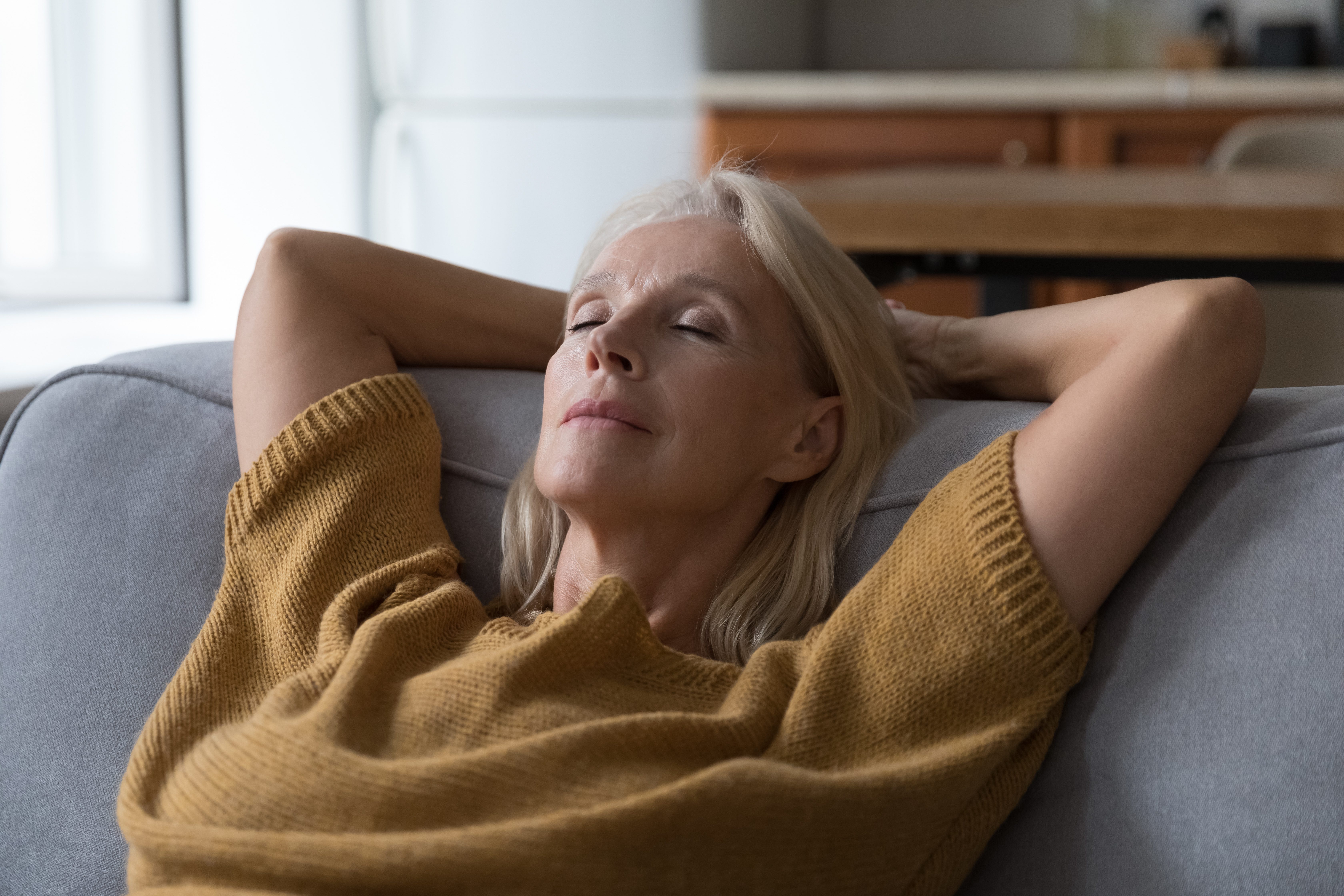 Peaceful middle aged woman resting on sofa with closed eyes